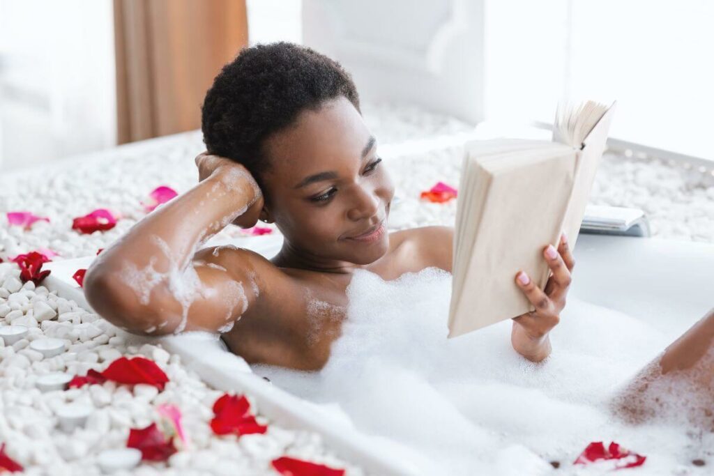 beautiful black woman lounges in bathtub readding self-care Sunday quotets for inspiration and motivation.