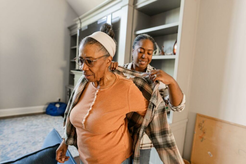 a middle aged daughter helps her elderly mother get dressed in senior adaptive clothing.