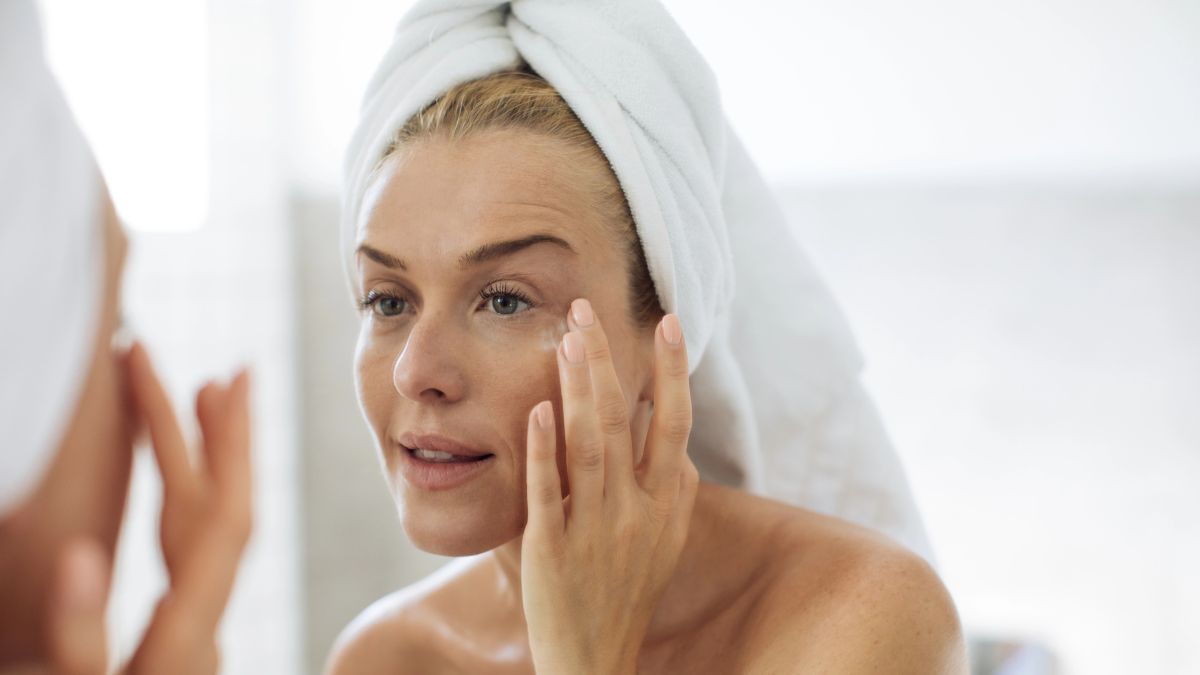 woman putting cream on face in mirror