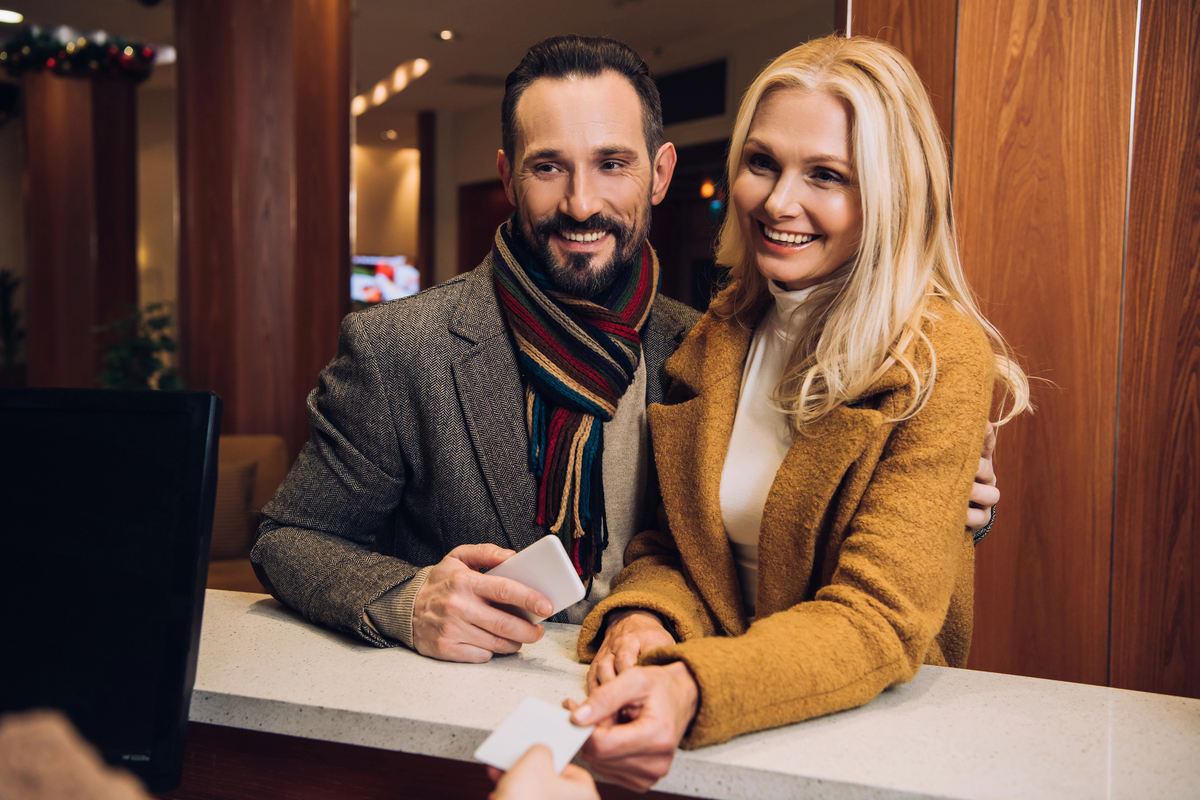 Smiling mature couple holding smartphone and card at reception in hotel