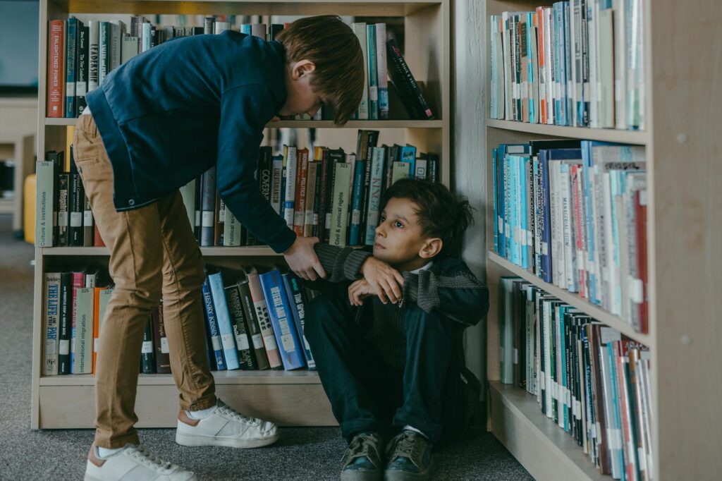 A_concerned_boy_interacting_with_a_classmate_sitting_on_the_floor_in_a_library..Mikhail_Nilov