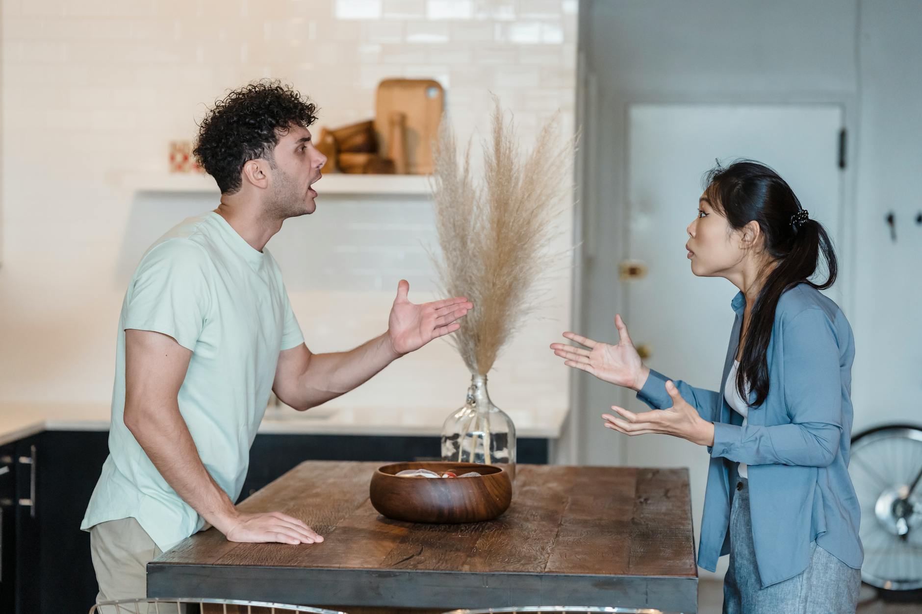 A couple engages in a heated argument at a wooden table in a modern indoor setting.Timur Weber