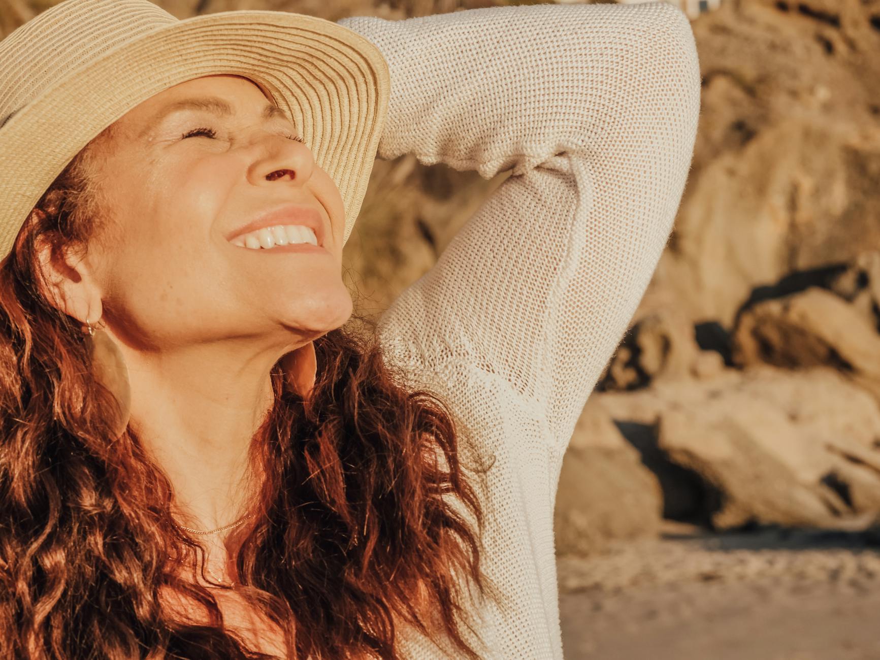A joyful woman with a hat basks in the sunlight by the seaside symbolizing relaxation and happiness.Kindel Media 1