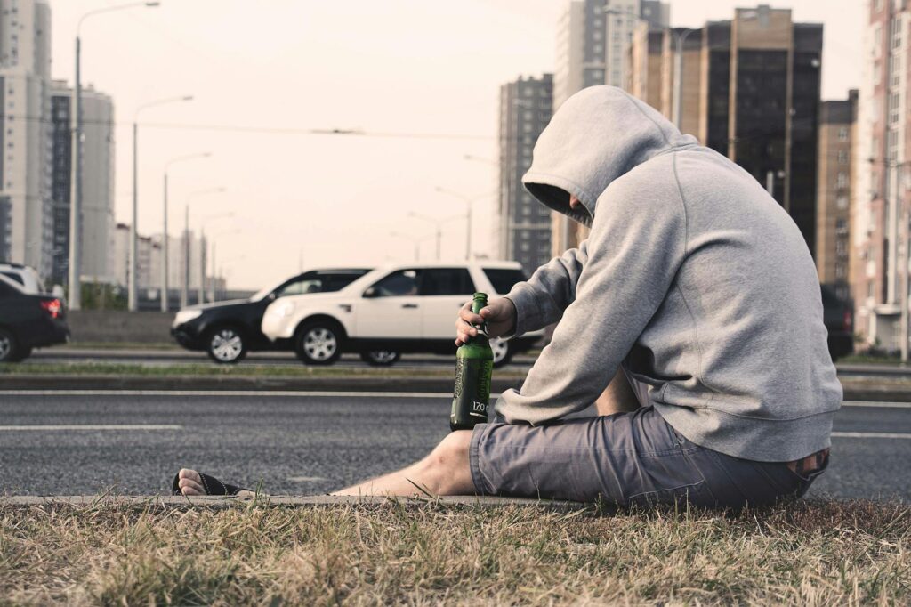 A man sits alone on the roadside in Moscow, holding a beer, reflecting urban loneliness.