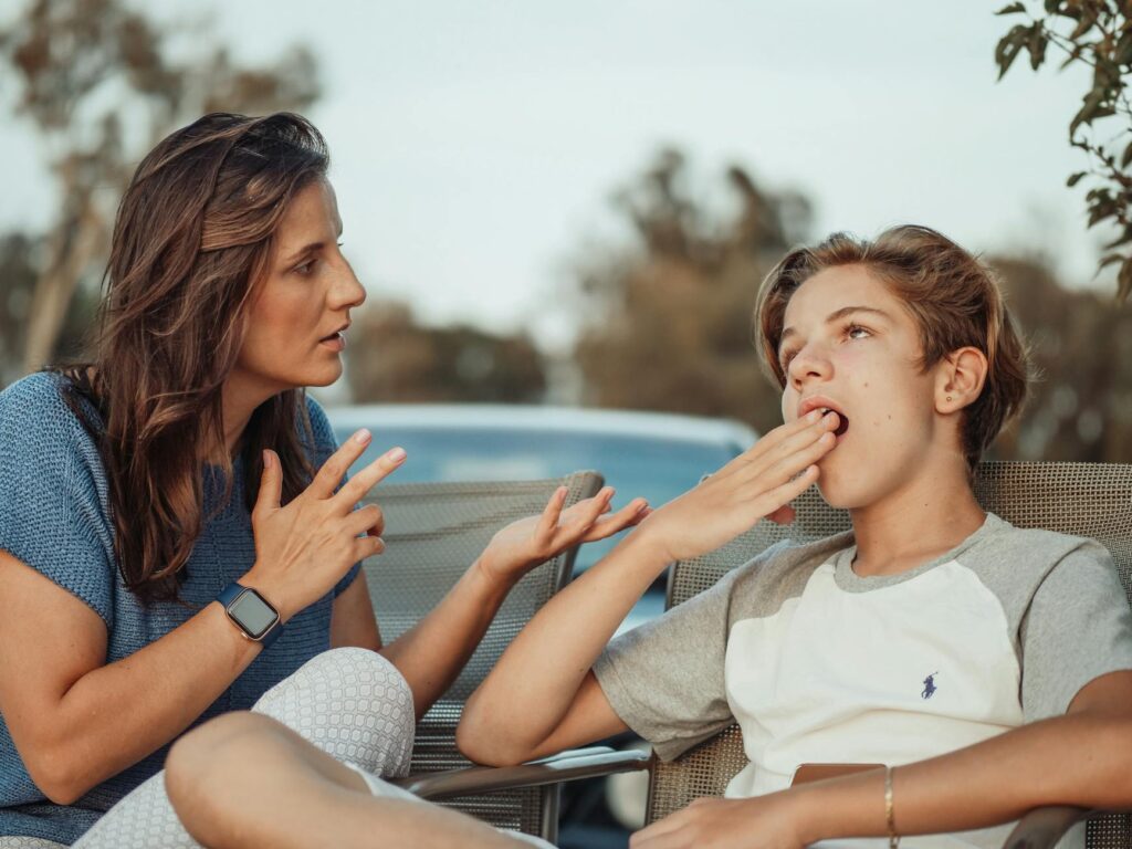 A_mother_and_her_teenage_son_are_having_a_conversation_outdoors._The_son_appears_disinterested..Kindel_Media