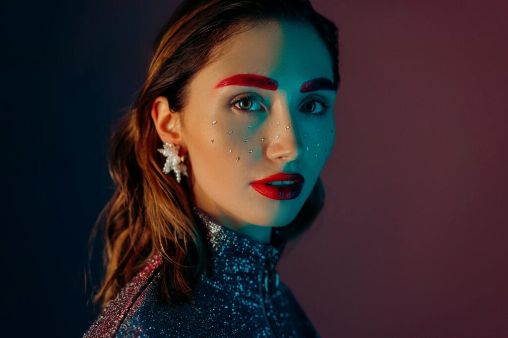 A striking portrait of a woman with vibrant makeup, glitter, and jewels, showcasing fashion and beauty creativity.