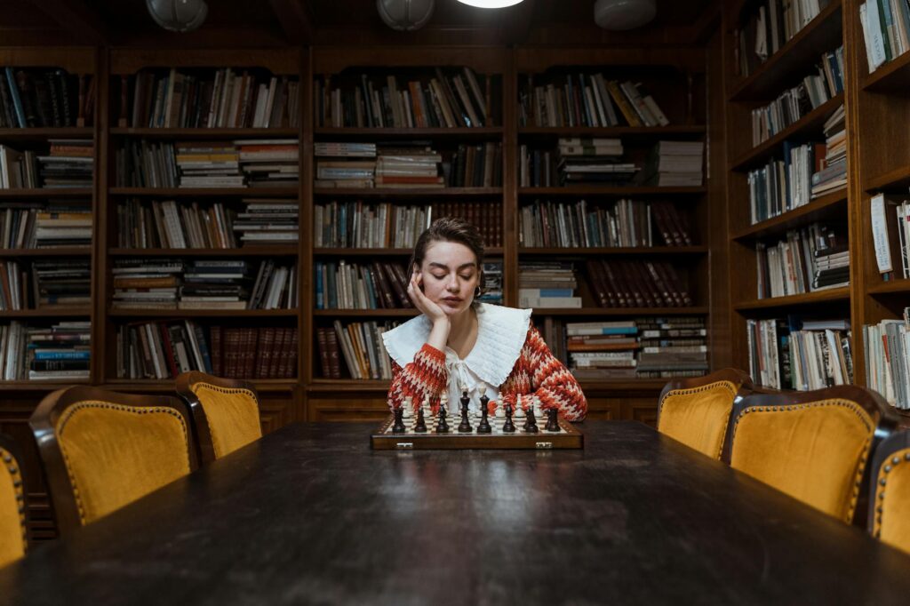 A woman contemplating her next chess move in a cozy library setting.