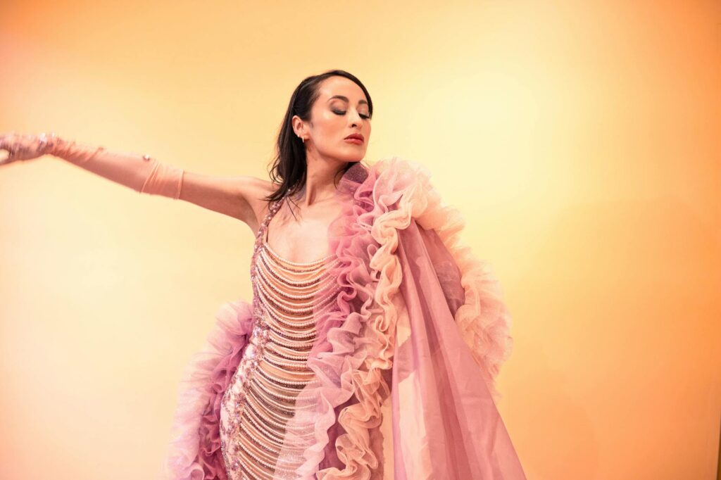 A_woman_gracefully_poses_in_a_ruffled_pink_gown_against_a_warm_pastel_background..Azahel_Calzada_De_La_Luz