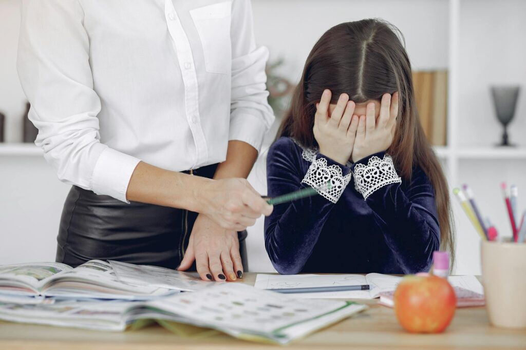 A_young_girl_overwhelmed_by_homework_with_a_teacher_assisting_her_indoors..Gustavo_Fring