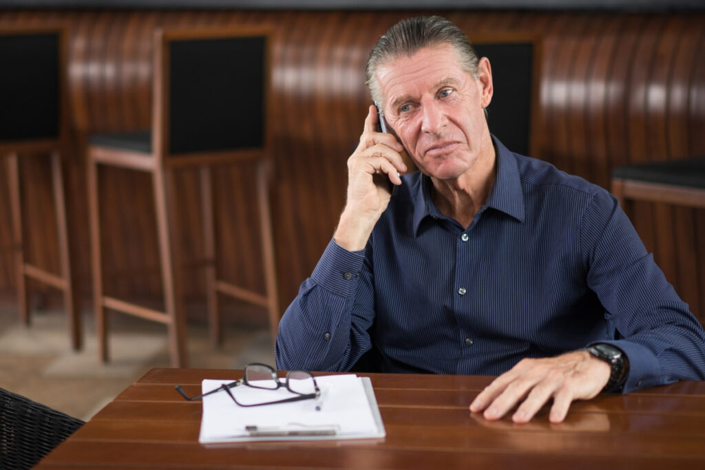 Serious Senior Man Talking on Phone in Restaurant