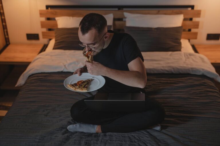 Man in Black Crew Neck T-shirt Eating on Bed