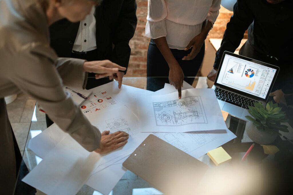 Business professionals collaborating over architectural drawings and graphs on a modern office desk.