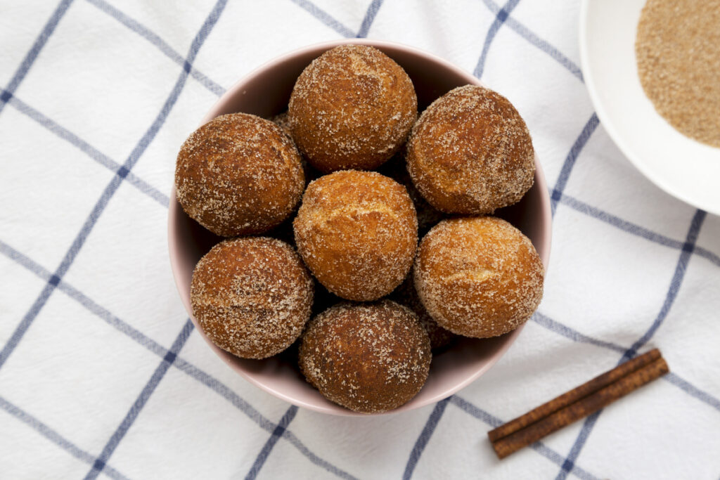 Homemade Fried Donut Holes in a pink bowl on cloth, top view. Flat lay, overhead, from above.