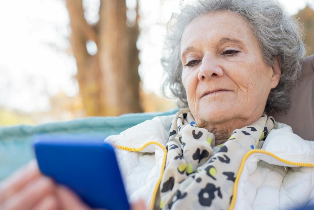 Elderly_woman_with_a_smartphone_relaxing_outdoors_in_autumn..Kampus_Production