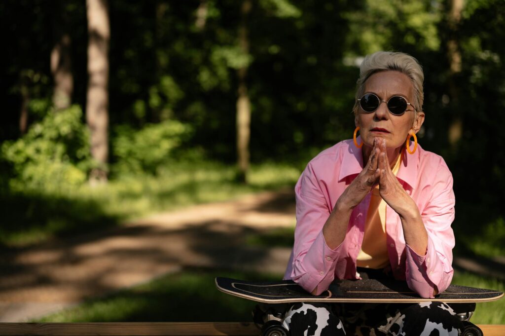 Elderly woman with sunglasses sits in park with skateboard exuding confidence and style.SHVETS production