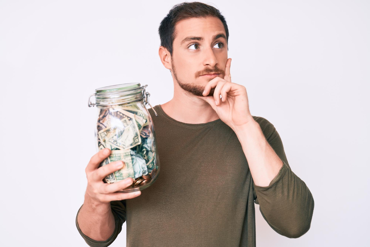Young handsome man holding jar with savings serious face thinking