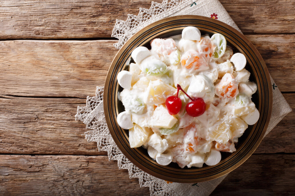 fruit salad Ambrosia from pineapple, tangerine, grapes and marshmelow close-up on a plate. Horizontal top view from above