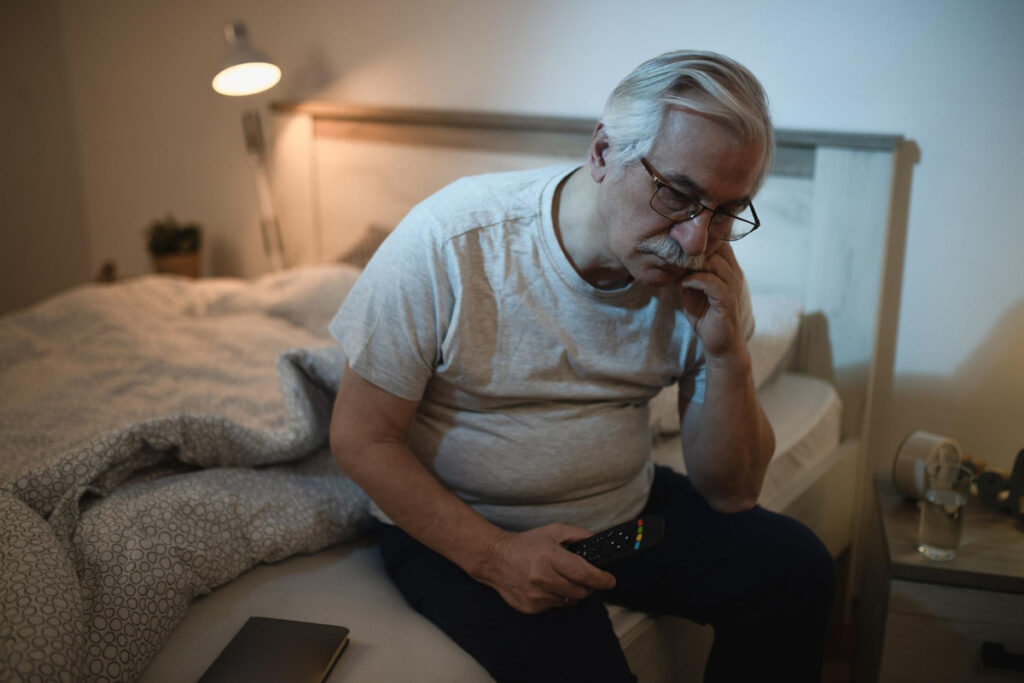 Sleepless mature man contemplating while sitting on the ned at night