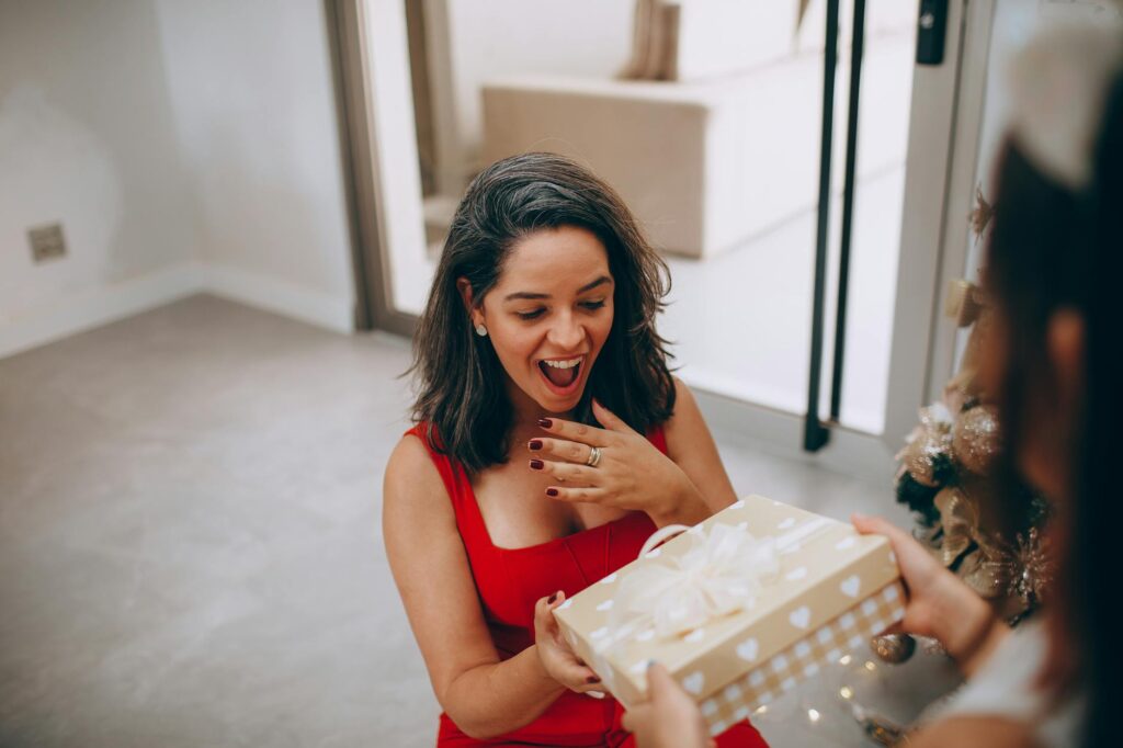 Woman in red dress excited to receive a Christmas gift indoors.