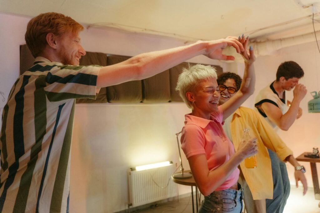 Lively scene of friends dancing and enjoying drinks at a casual indoor gathering.