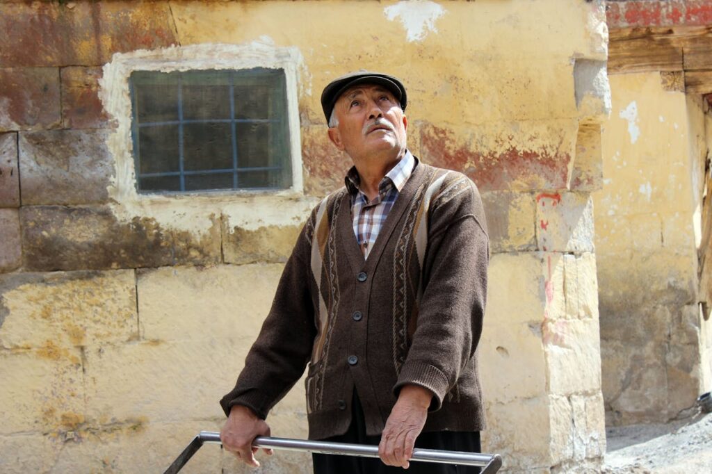 An Elderly Man in Brown Knitted Sweater Looking Up while Standing on the Street
