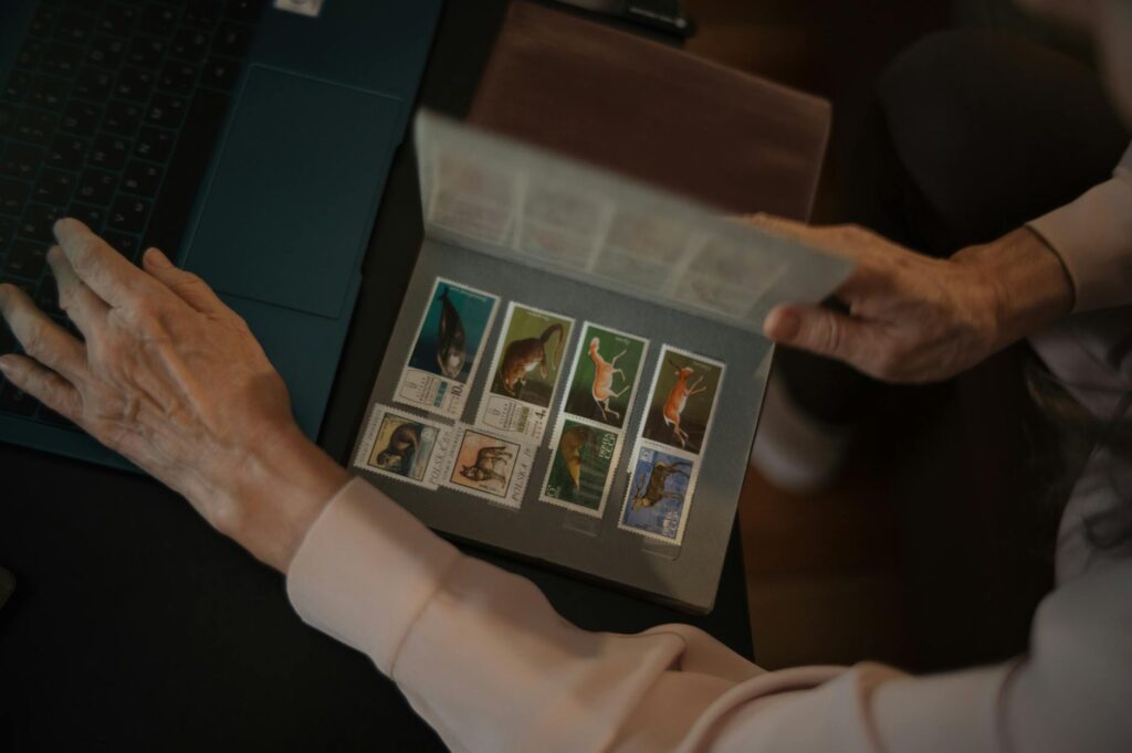 Senior adult using laptop while sorting a colorful stamp collection indoors.Mikhail Nilov