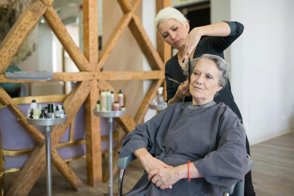 Senior woman gets a haircut from a hairstylist in a salon with wooden decor. Indoor setting.