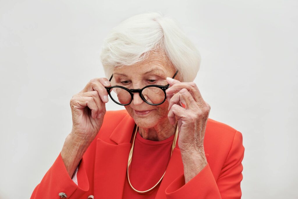 Senior_woman_in_coral_red_suit_adjusting_eyeglasses_with_focus_and_elegance..Moe_Magners