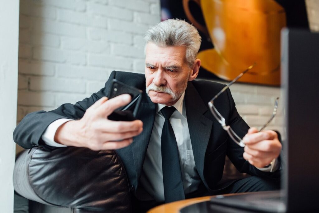 Middle-aged unhappy businessman in modern restaurant using laptop and phone.