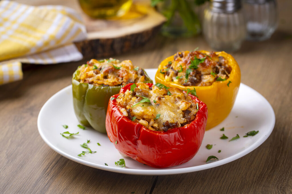 Stuffed peppers, halves of peppers stuffed with rice, dried tomatoes, herbs and cheese in a baking dish on a blue wooden table, top view. (Turkish name; biber dolmasi)
