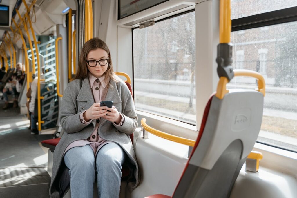A Woman in Gray Coat Sitting inside a Tram while Using a Cellphone