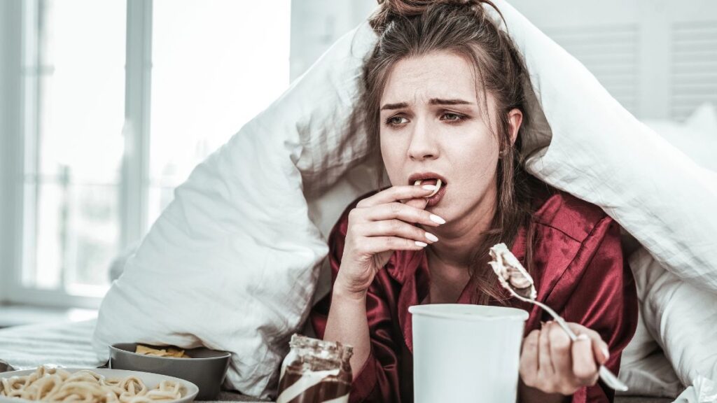 depressed woman eating junk food in bed