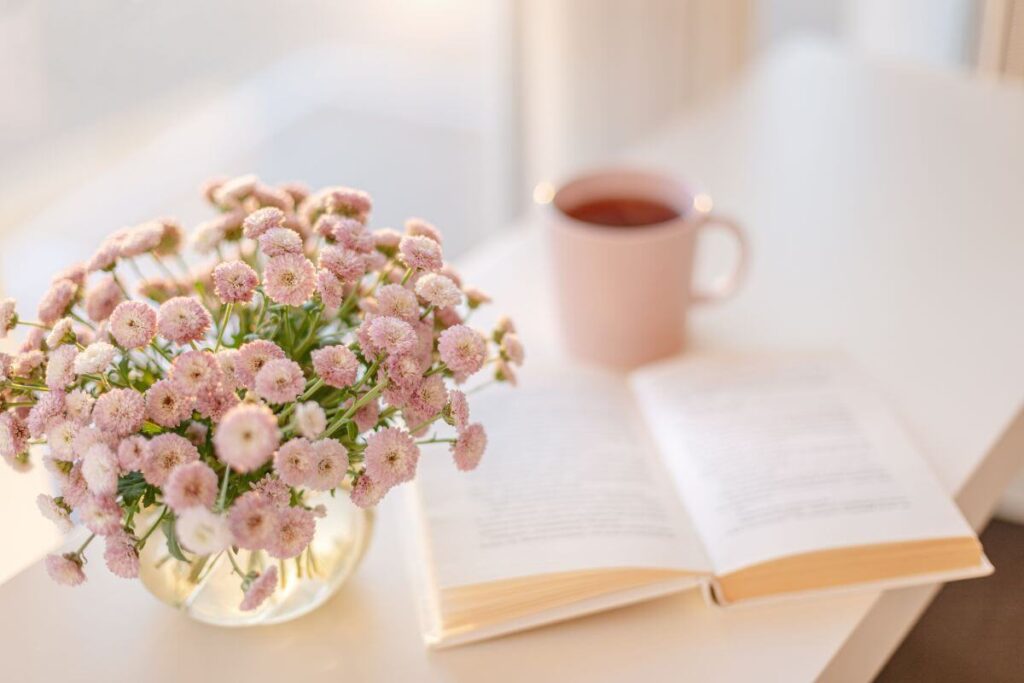 pink flowers in a round vase, a book, and a pink mug sit on a shelf for a nice self care weekend.