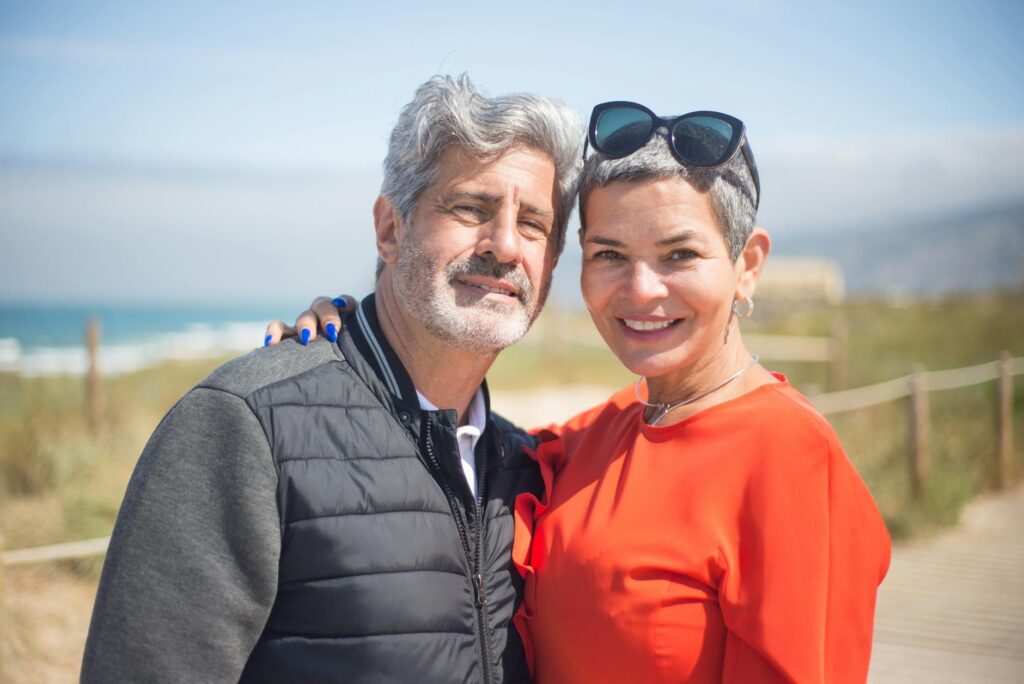 A joyful senior couple smiling together at a sunny beach in Portugal.Kampus Production