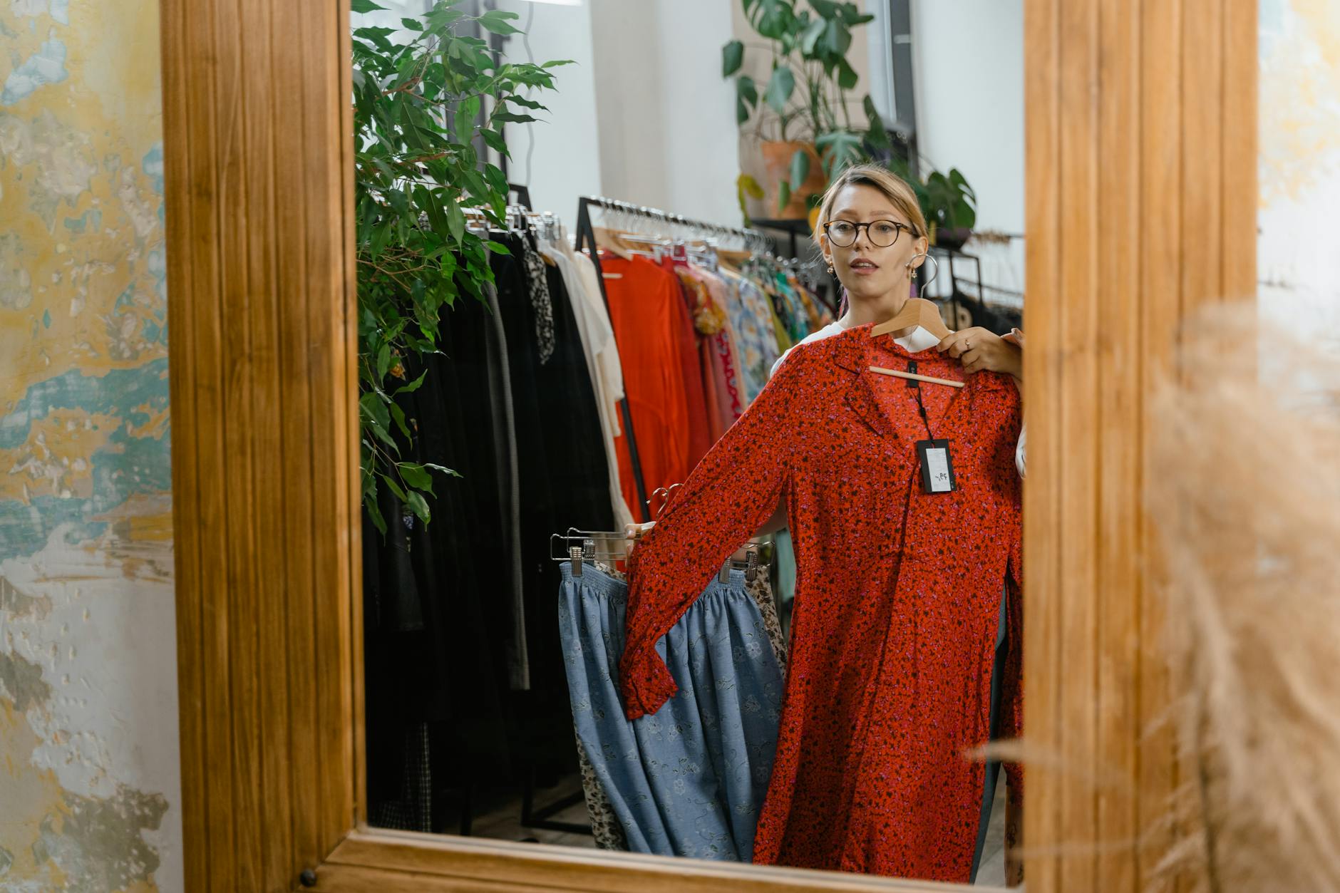 A woman stands in a boutique viewing a red dress in a mirror showcasing fashion choices.MART PRODUCTION