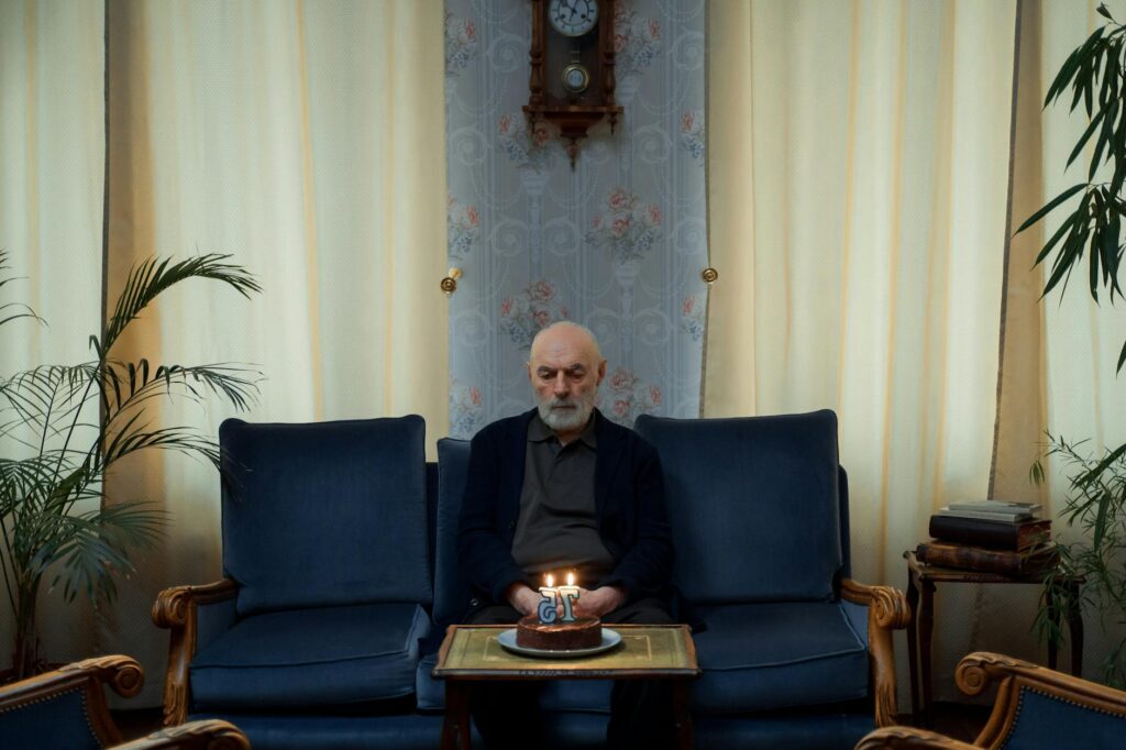 An elderly man sits alone with a lit birthday cake indoors suggesting contemplation and solitude.cottonbro studio 1