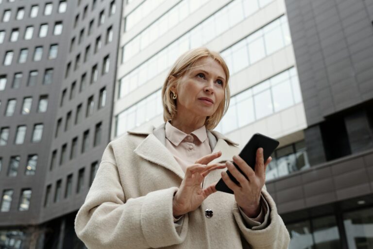 Businesswoman in a coat using a smartphone outside office buildings.