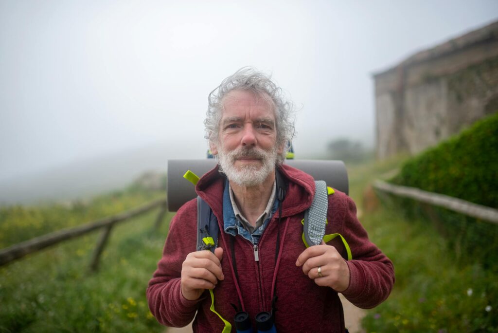 Elderly man hiking with backpack on a misty trail in Portugal, capturing the spirit of outdoor adventure.