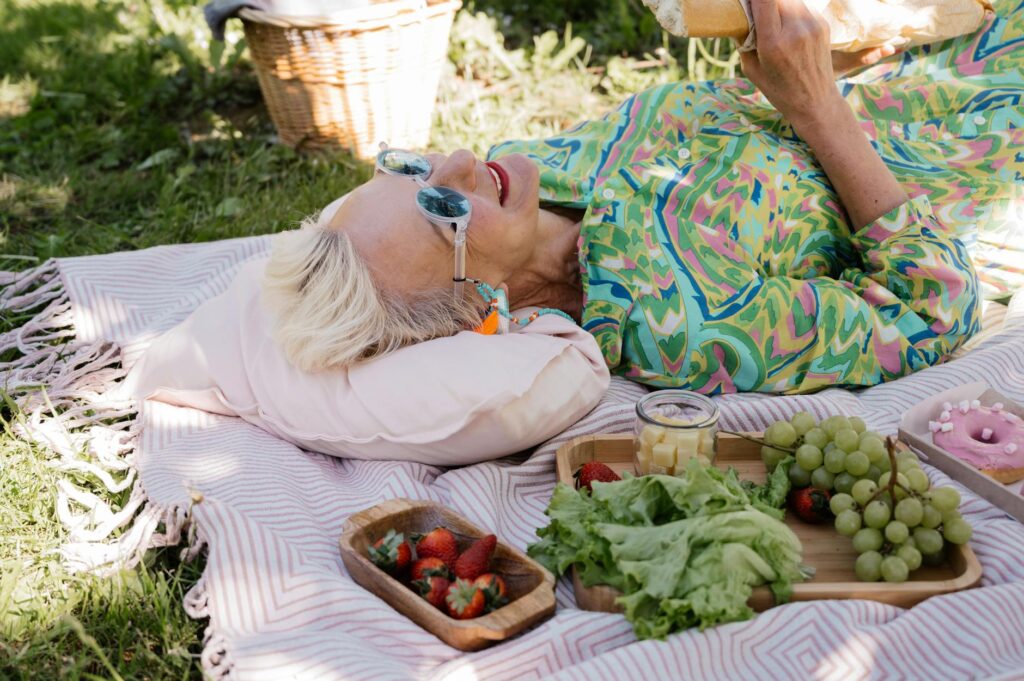 Elderly woman relaxing with picnic items on a sunny day showcasing joy and leisure.SHVETS production