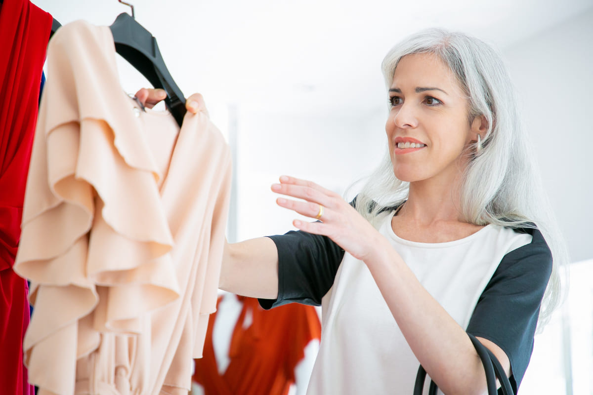 Happy clothes shop customer taking hanger with dress from rack for trying. Woman choosing clothes in fashion store. Consumerism or retail concept