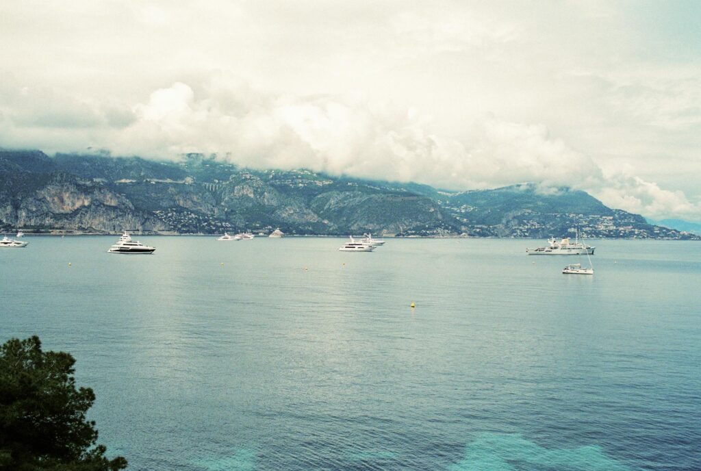 Scenic view of luxury yachts anchored along the stunning French Riviera coastline under a cloudy sky.
