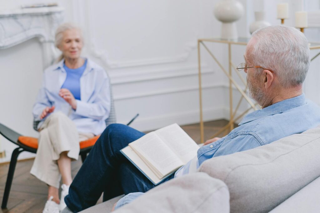 Senior adults sitting on a sofa enjoying a peaceful moment with a book and conversation.SHVETS production
