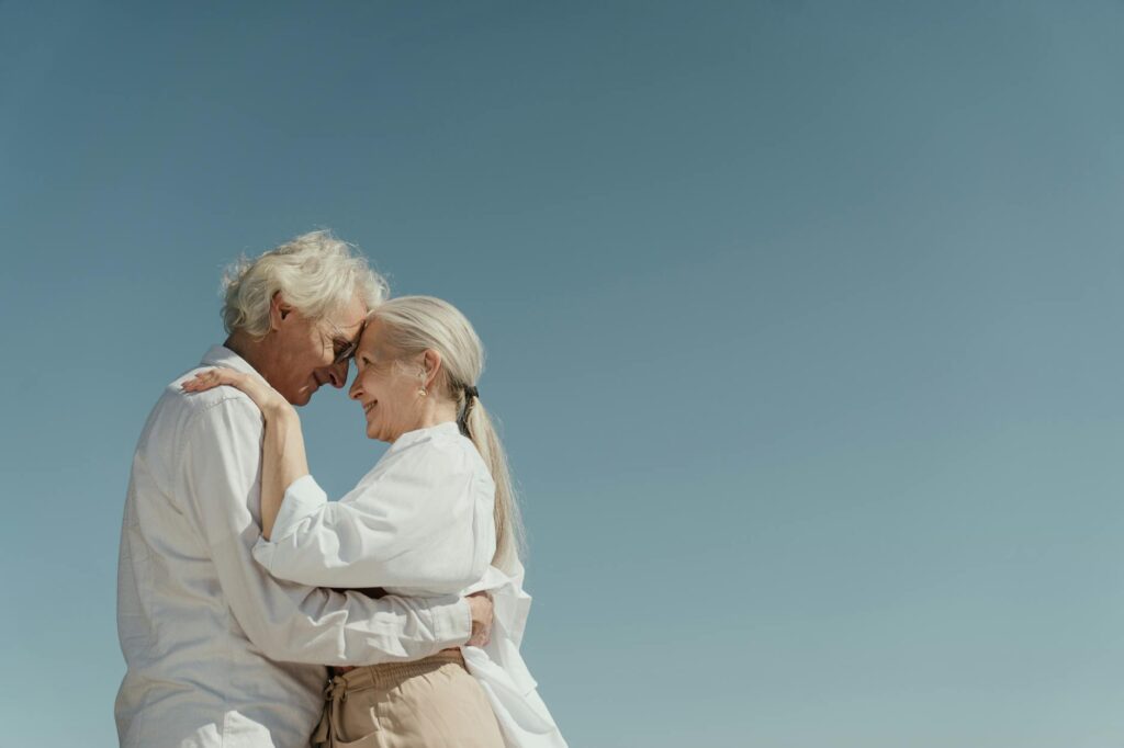 Senior couple embracing outdoors depicting love and happiness against a clear blue sky.cottonbro studio
