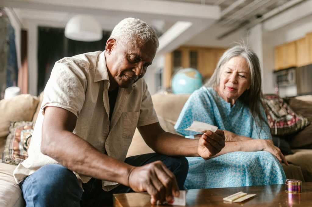 Senior couple sitting on a sofa, engaging in rolling legal marijuana indoors. Bright and relaxed atmosphere.