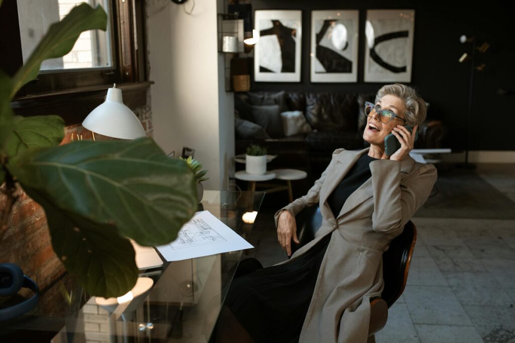 Senior woman in a modern office setting smiling while on a phone call. Stylish and professional workspace.RDNE Stock project