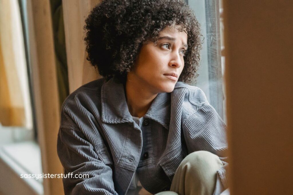female sits on a windowsill sadly looking out an pondering how to respond when someone says you are too sensitive.