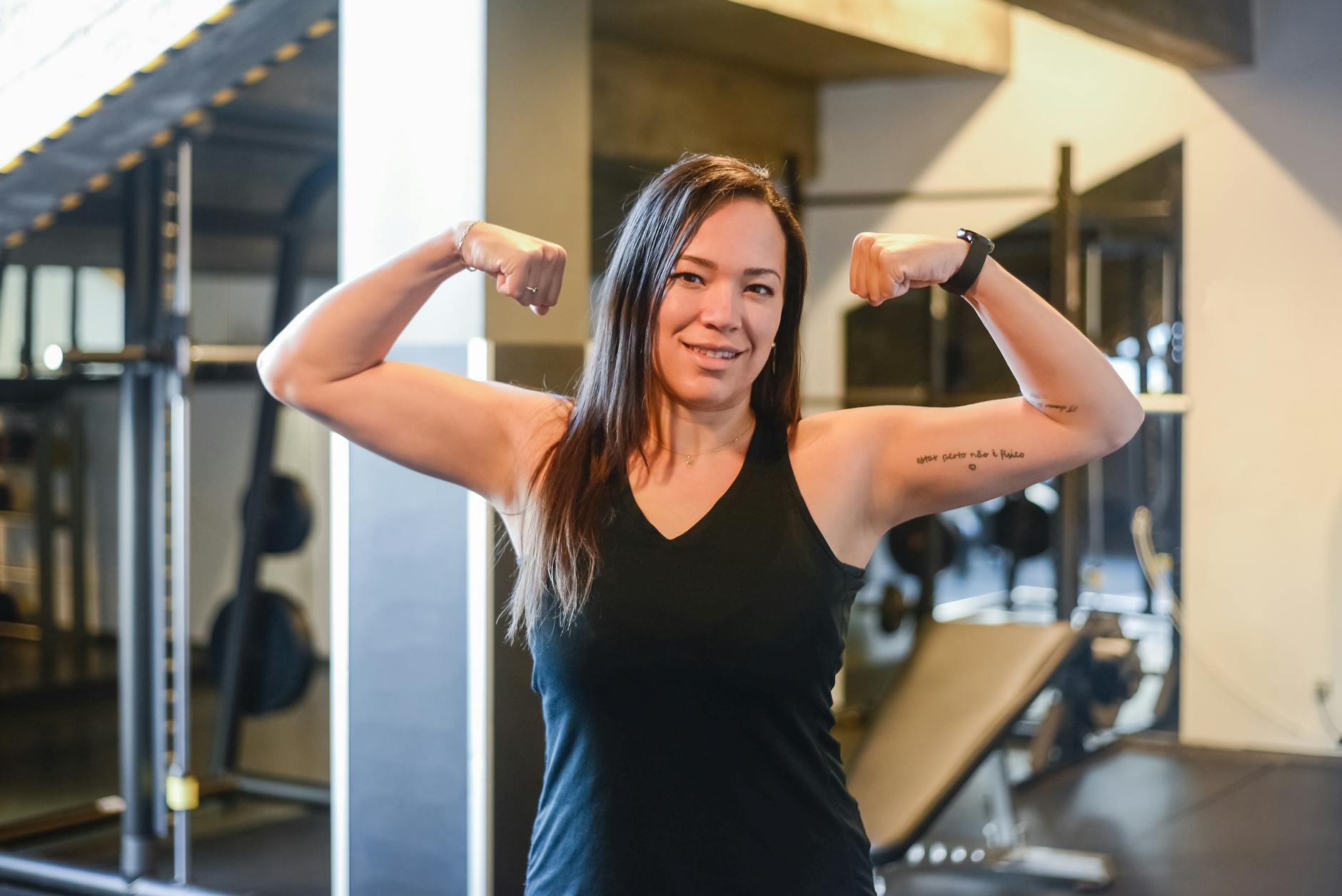 Strong woman in a black tank top confidently flexing her muscles in a gym setting smiling.Kampus Production 1 1