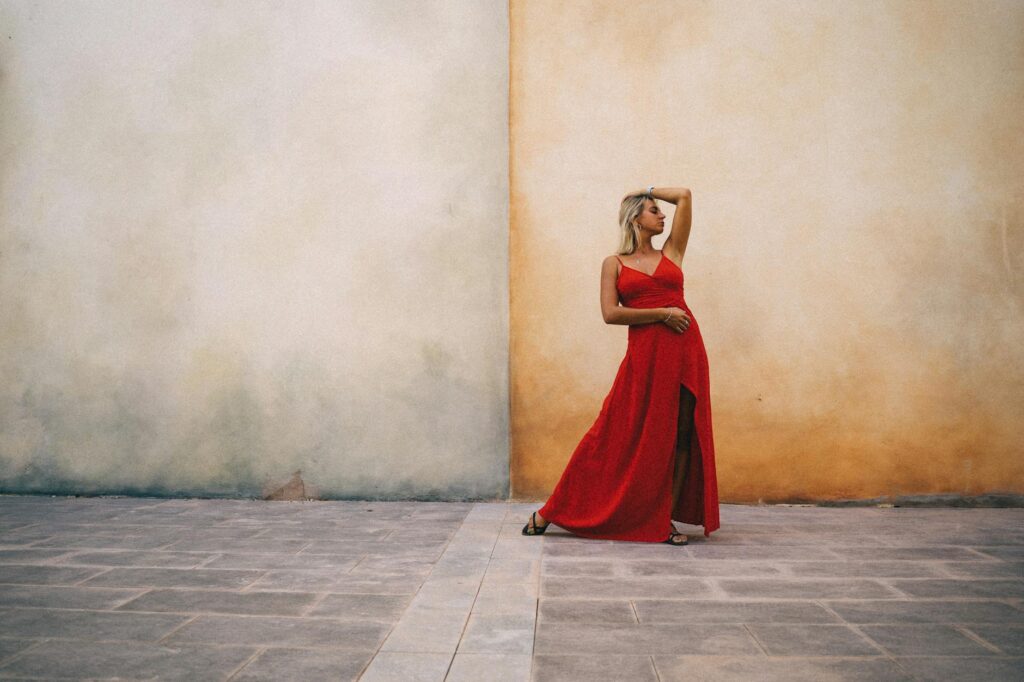 Stylish woman in vibrant red dress poses against a rustic wall exuding confidence and grace.Anna Tarazevich