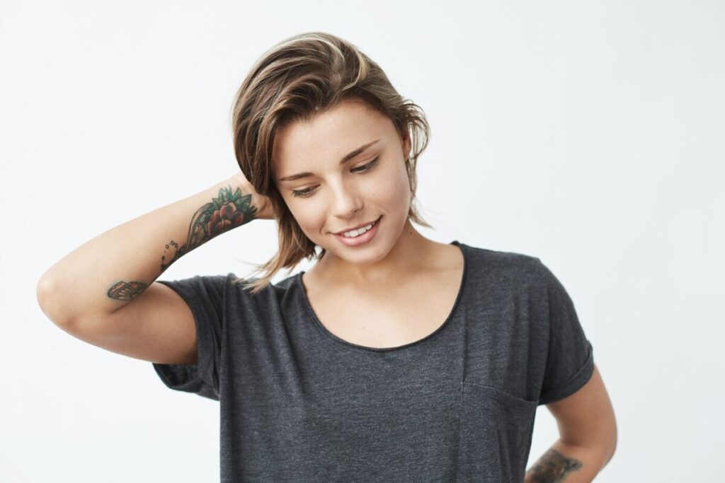 Shy young pretty tattooed girl smiling looking down.