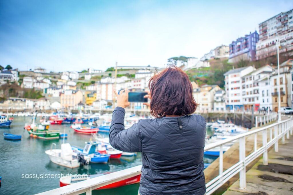 middle aged female traveler snapping a photo of the harbor outside her hotel.